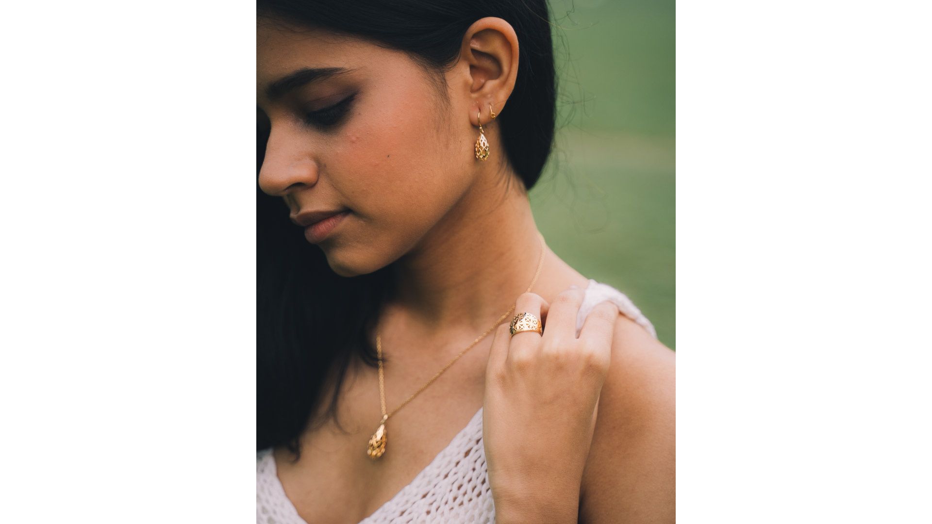 A person wearing a white top and gold necklace
Description automatically generated
